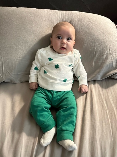 Baby Benny propped up on the couch, wearing green paints and a clover top.