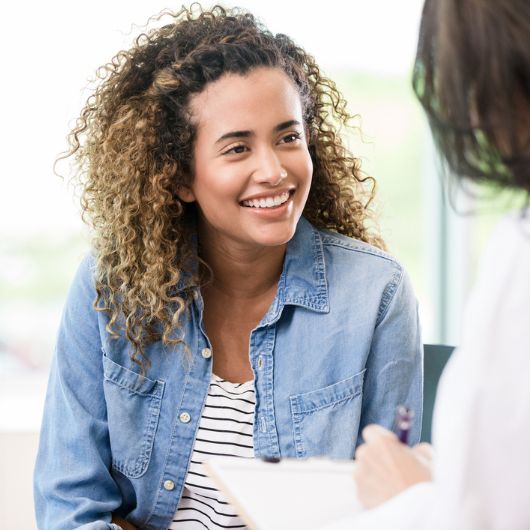 A smiling female patient attentively listens as a doctor gives her good news.