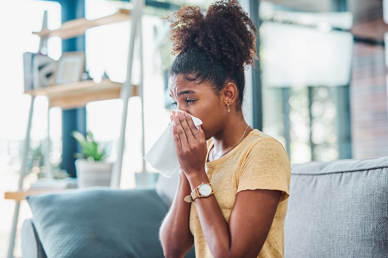 Woman blowing her nose on the couch not feeling well - allergies or a cold