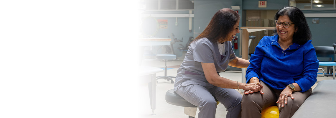 Physical therapist laughing with the patient sitting on a yoga ball while laughing and holding each others hands