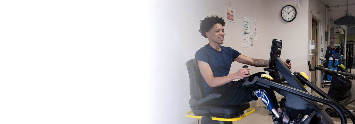 Smiling patient with a prosthetic leg sitting on an exercise machine