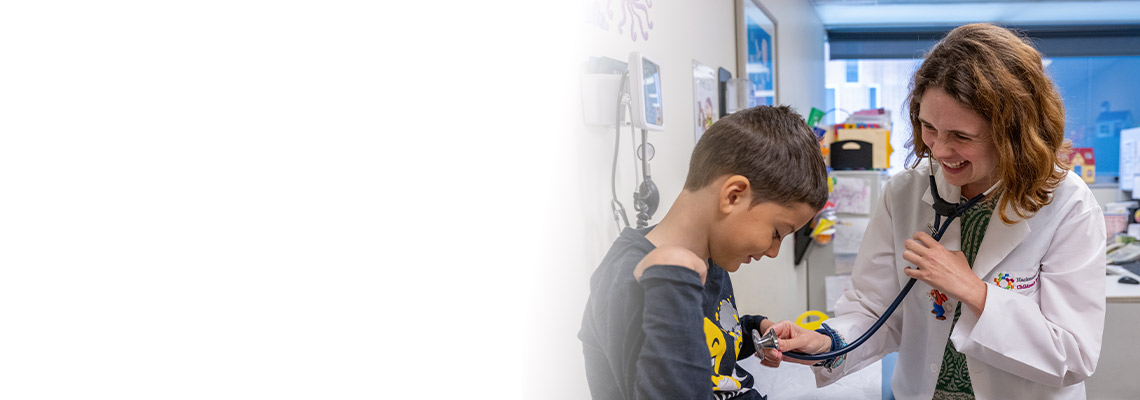 Pediatrician smiling with a young patient and holding a stethoscope to his chest