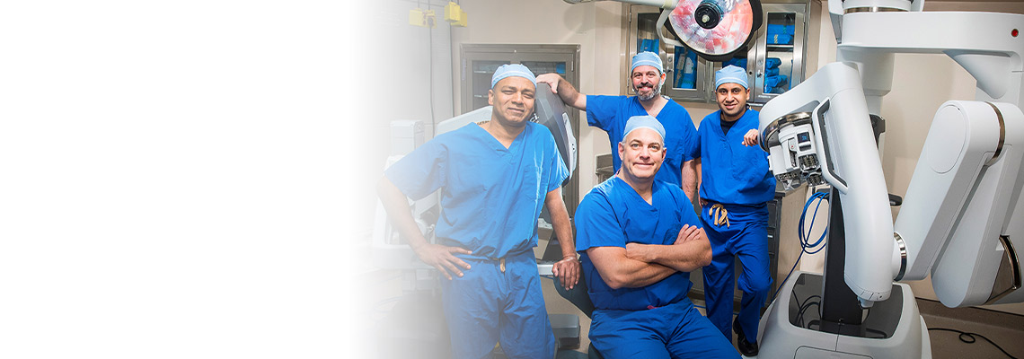urologic surgery team in blue scrubs standing in front of single port robotic surgery machinery