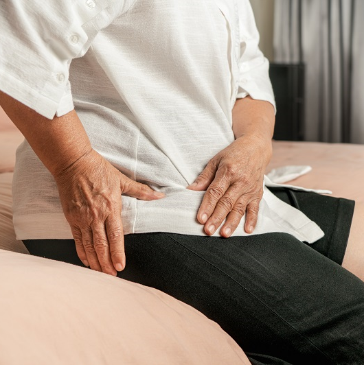 Older woman, sitting down and holding her hip from pain.