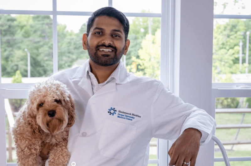 Tarun Kakumanu, D.O., holds his dog while leaning up against a step ladder.