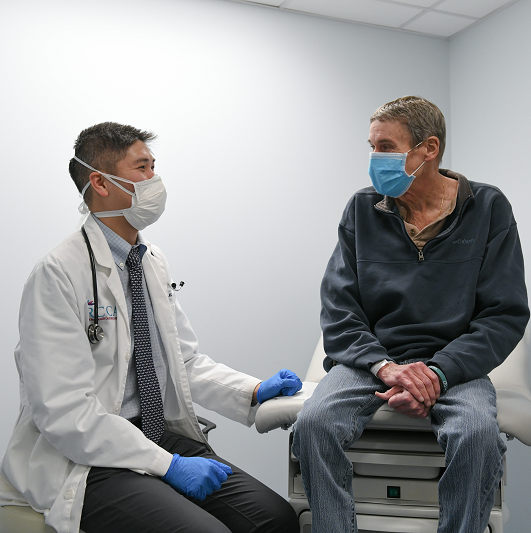 Male patient sitting with a doctor in a patient room talking and smiling.
