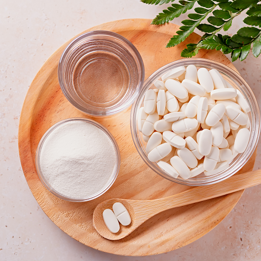 Collagen powder, pills and glass of water on wooden tray