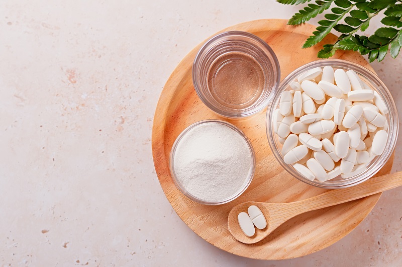 Collagen powder, pills and glass of water on wooden tray