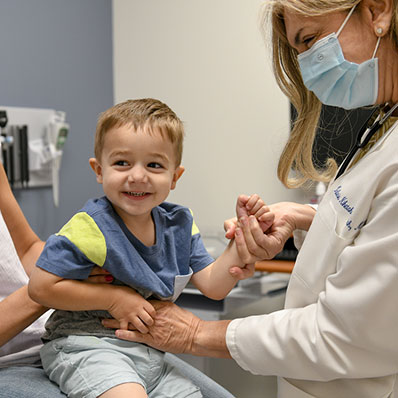 little boy smiling, sitting on mother's lap while interacting with the pediatrician