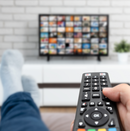 Man laying on sofa, binge watching TV with remote control in his hand.