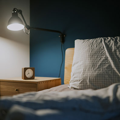 bedroom at night illuminated by electric lamp with clock on night table beside the bed with blue wall