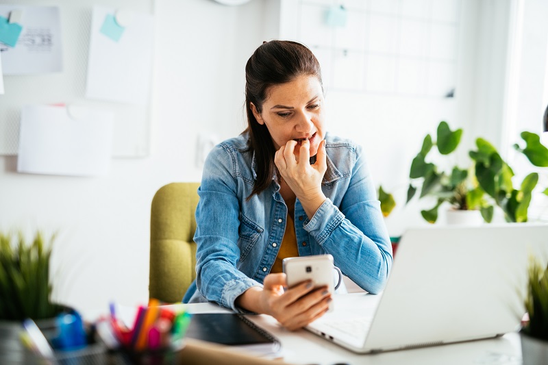 Anxious woman, biting her nails and working in office and using smart phone