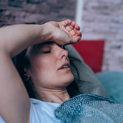 Woman woken up at night from night sweats. Has her hand on her forehead to feel the warmth.