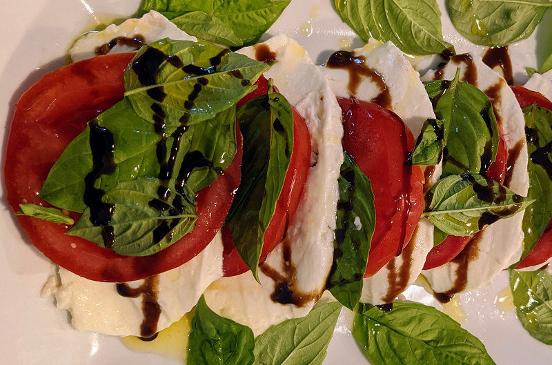Caprese salad on a plate - tomatoes, mozzarella, and vinaigrette drizzle.