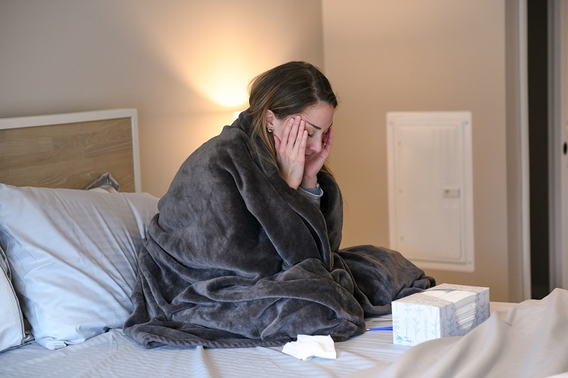 Young woman sick in bed with a headache, possibly COVID from a COVID exposure.