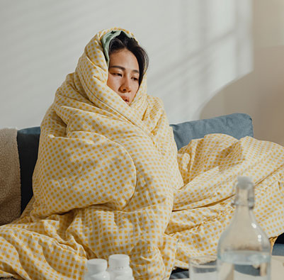 Young woman sick on the couch, wrapped up in a blanket, shivering from the flu and body aches.