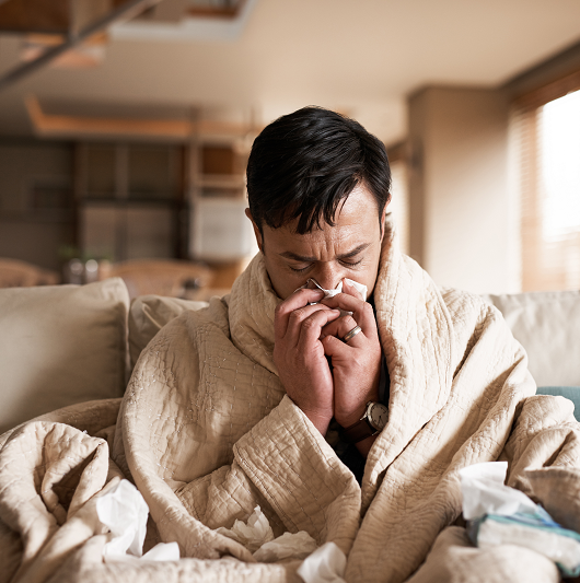 Man at home sick with the flu on the cough blowing his nose with a tissue