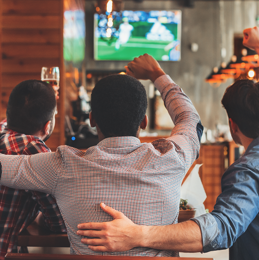 Three men watching football on TV in sport bar, back view