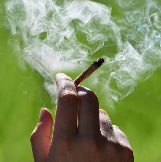 Hand holding a marijuana joint with smoke around it.