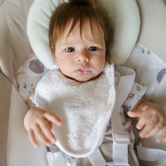 Baby with a bib spitting up after a bottle of milk