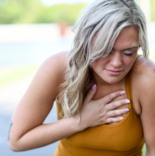 Young woman with blonde hair clutching her chest in pain, suffering from heart burn