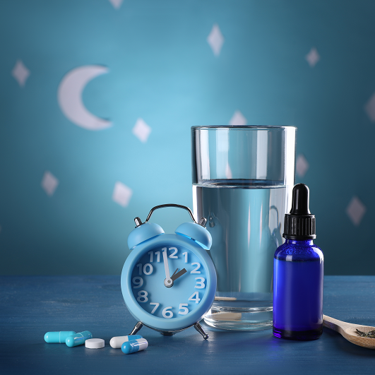 Alarm clock and different remedies for insomnia treatment near glass of water on table against blue wall decorated with stars and crescent