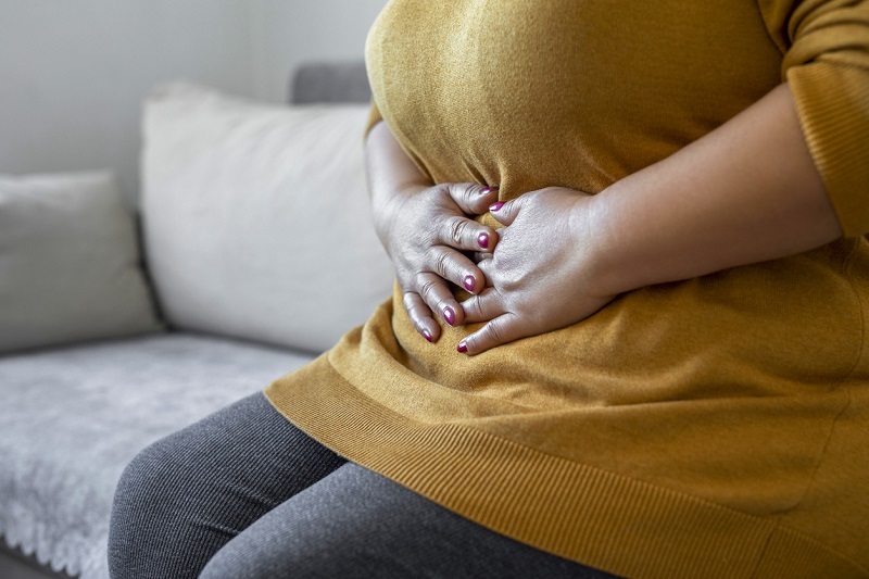 Woman holding her stomach with her hands, while sitting on the couch.