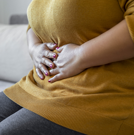 Woman holding her stomach with her hands, while sitting on the couch.