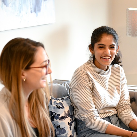 Two friends sitting in the living room smiling and hanging out together.