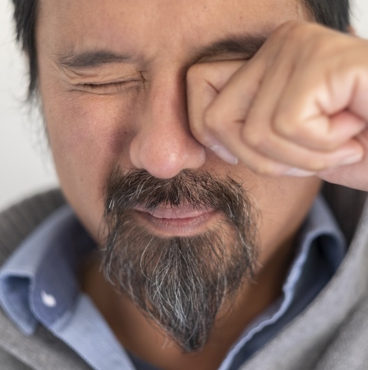 Close up shot of man with an eye floater rubbing his eye due to an eye floater.