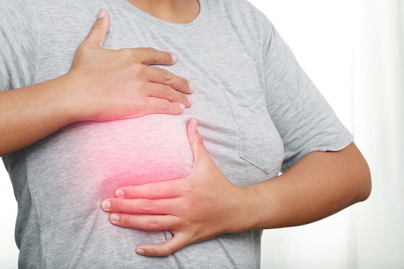 A woman in a gray shirt holding her breast feeling for a breast cancer lump.