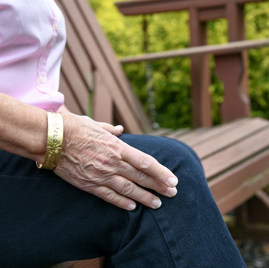 Woman sitting on a bench outside, holding her knee in pain. Suffering from joint pain and considering a cortisone shot.