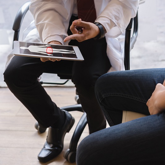 Doctor sitting with a patient discussing prostate cancer symptoms, looking at an iPad.