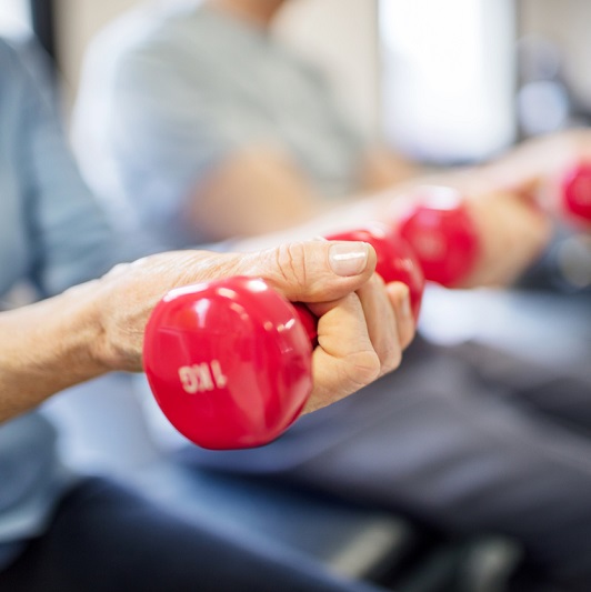 Midsection of senior woman lifting dumbbells for strength training.