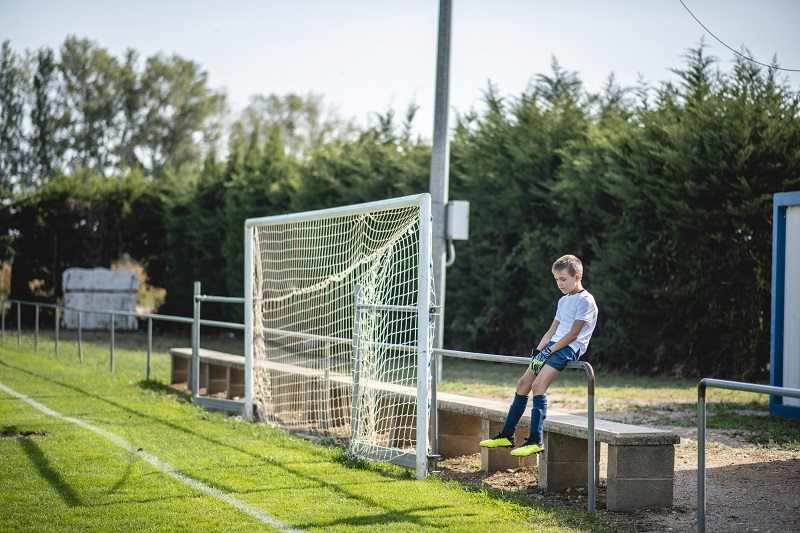Young soccer player sitting on a fence before a game, looking frustrated.