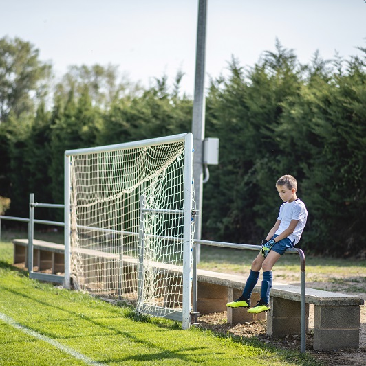 Young soccer player sitting on a fence before a game, looking frustrated.