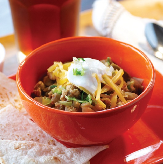 A red bowl of turkey chili - topped with sour cream and shredded cheese.