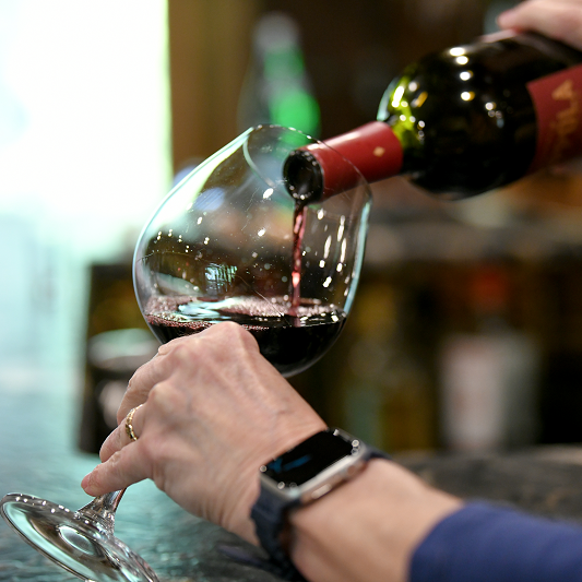 red wine being poured into glass by man wearing a watch