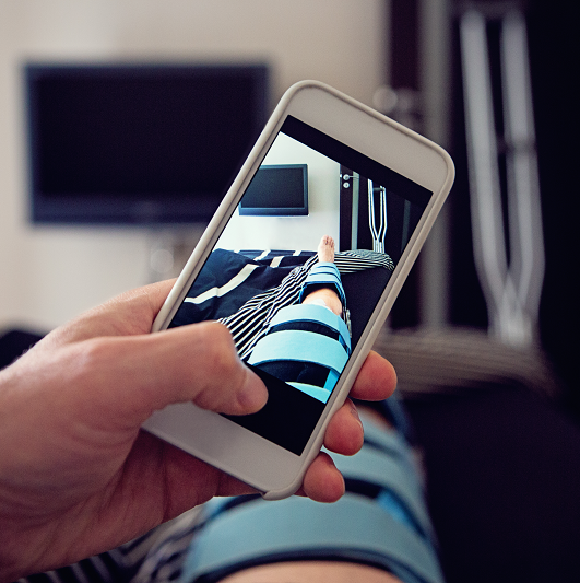 Man laying in bed taking a picture with his phone of his leg in a brace, recovering from ACL tear.