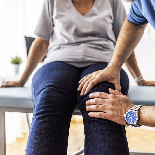 Doctor's hands on a patient's knee, evaluating for osteoarthritis.