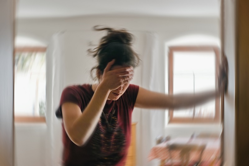 Woman standing, one hand on her forehead, one on the wall, trying to regain balance. Suffering from vertigo.