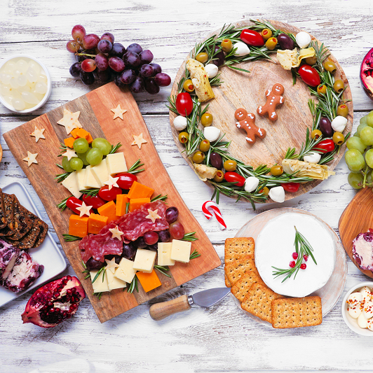 Christmas charcuterie table scene over a white wood background. Selection of cheese and meat appetizers. Christmas tree, wreath and candy cane arrangements.
