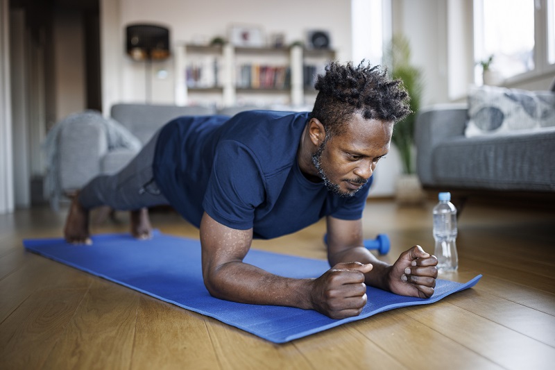 Man exercising at home doing planks to strengthen his back and ease pain caused by spinal stenosis.