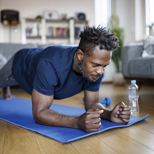 Man exercising at home doing planks to strengthen his back and ease pain caused by spinal stenosis.