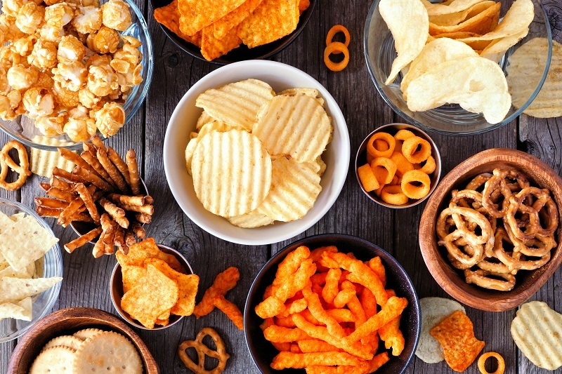 An assortment of chips and processed snacks in bowls on a table.