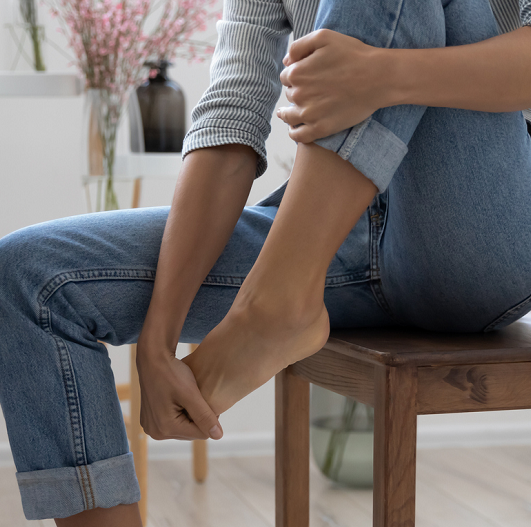 Close-up of a woman sitting on a chair, holding her toes from toe pain.