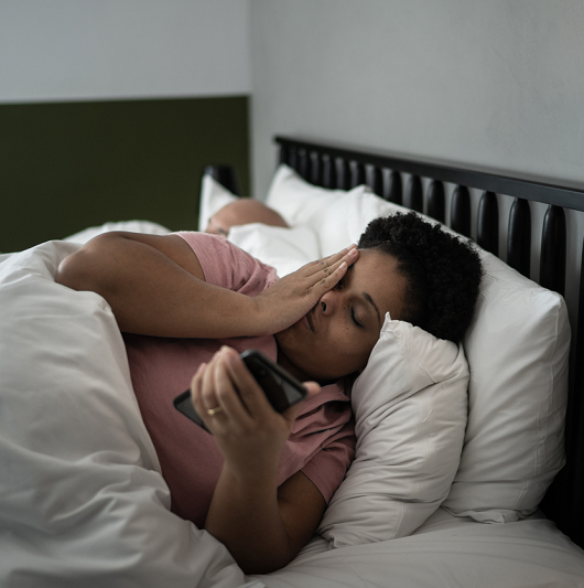 Woman laying in bed in the morning, checking her phone, looking tired.