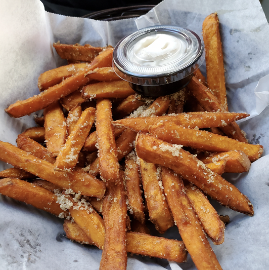 A basket of crisp sweet potato fries with a garlic yogurt dip on the side. A basket of crisp sweet potato fries with a garlic yogurt dip on the side.