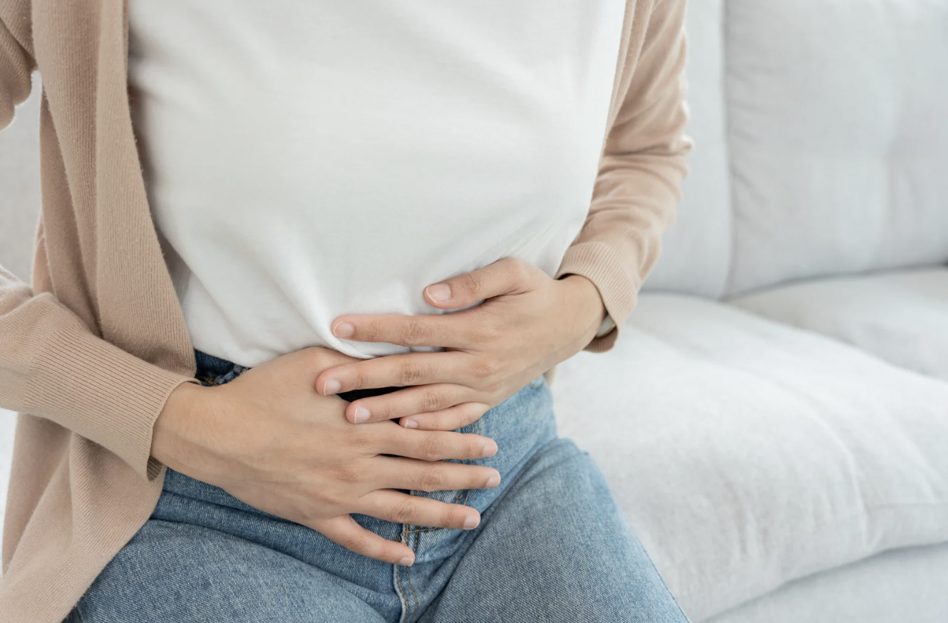 A woman sitting on a couch clutches her abdomen with both hands.