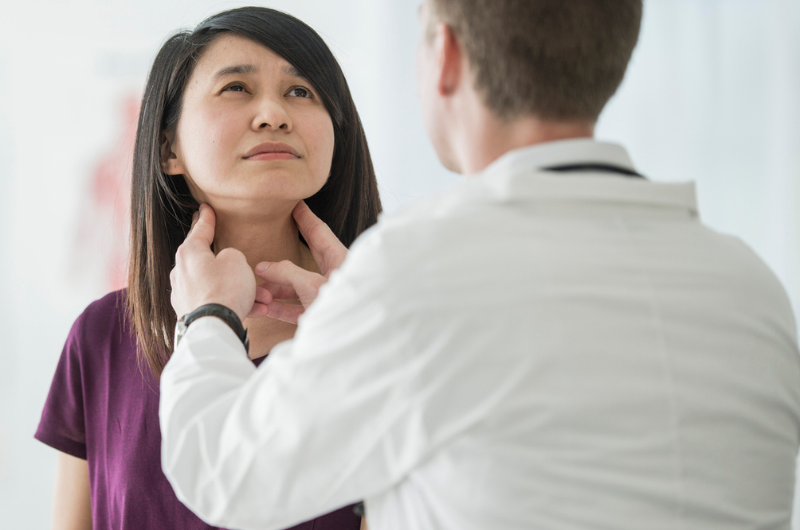 A Caucasian male doctor feels the swollen throat of a female patient. A Caucasian male doctor feels the swollen throat of a female patient.